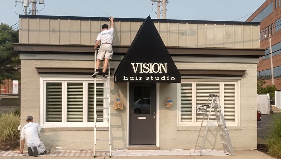 Painters working from ladders on a small commercial storefront exterior