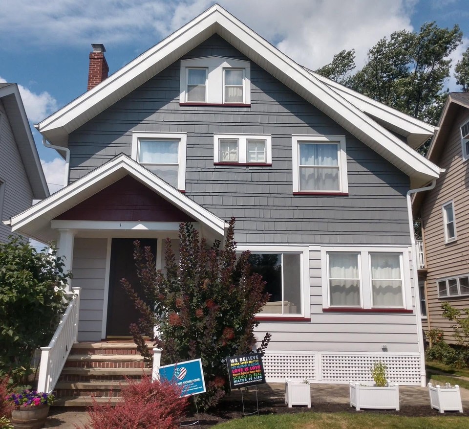 Completed gray gabled home exterior with crisp white trim and a red entry door
