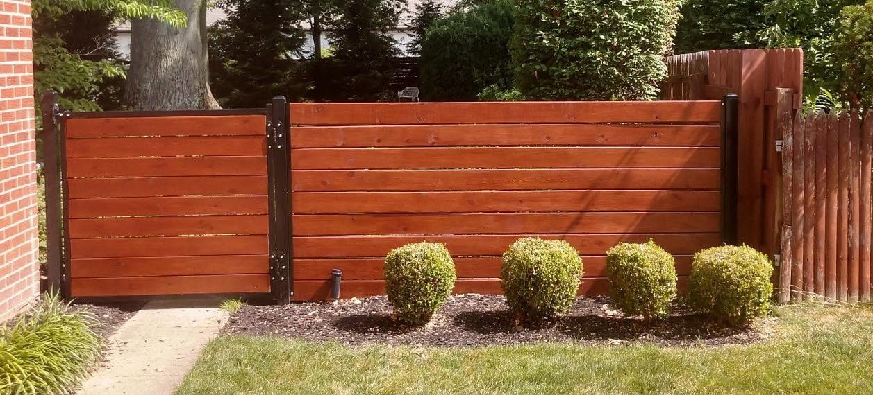 Completed stained wood fence and gate beside a brick building