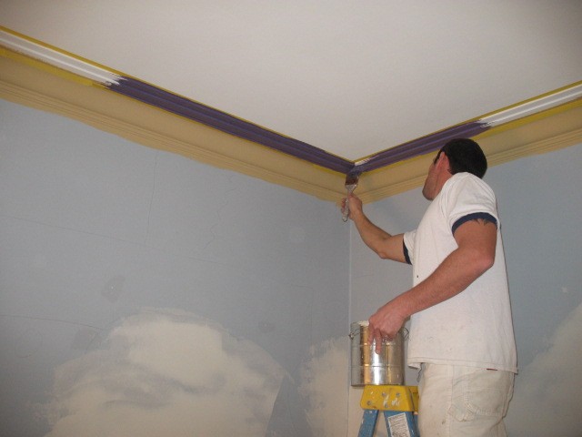 Painter working carefully along masked crown molding above a patched interior wall