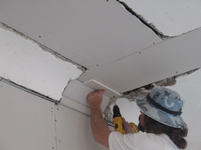 Painter cutting and preparing a damaged ceiling area for repair